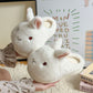 Pair of white bunny plush slippers with pink lined ears held in two hands in front of a printed poster