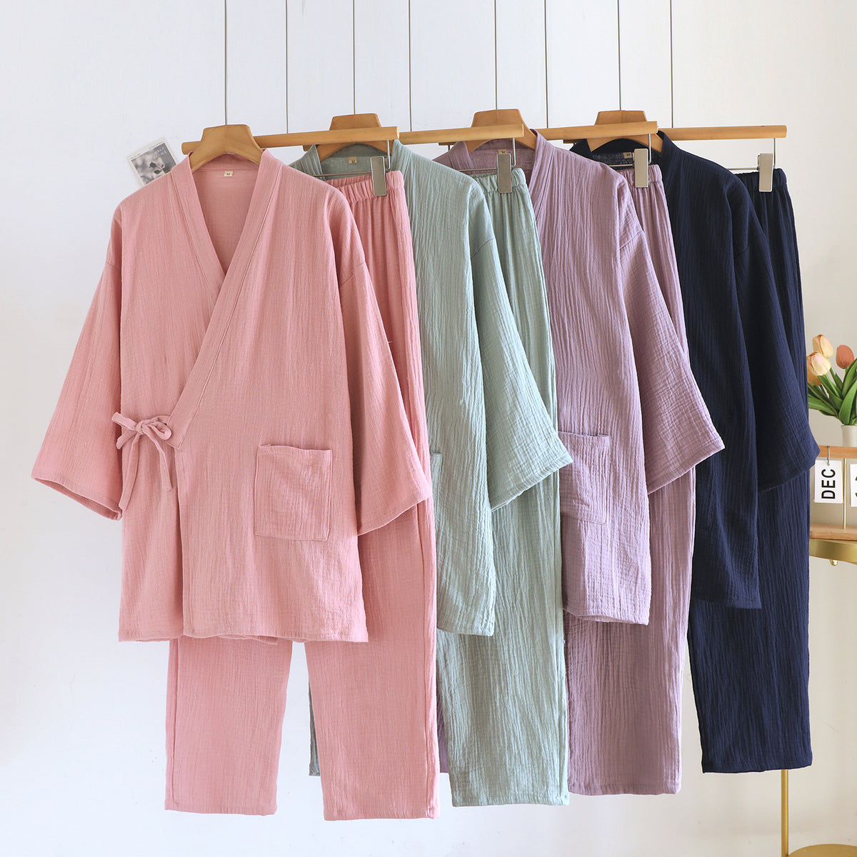 Pink, green, purple and navy kimono pajama sets hanging on hangers with wrap tops, side ties and patch pockets