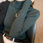 Model wearing a dark green slim ribbed semi high mock neck knit sweater tucked into trousers