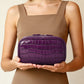 Woman holding a purple crocodile pattern cosmetic bag with both hands in front of her