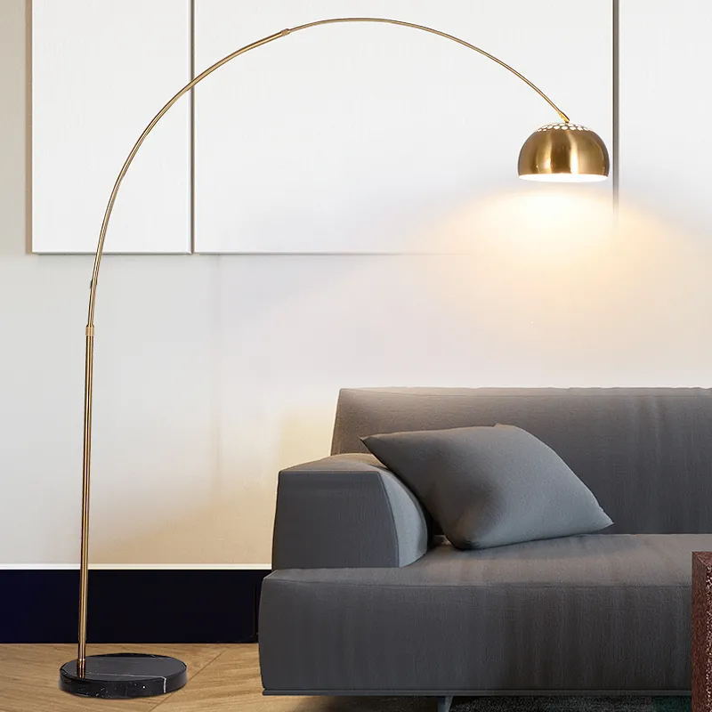 Gold arc LED floor lamp arching over a grey sofa with a dome shade and marble base