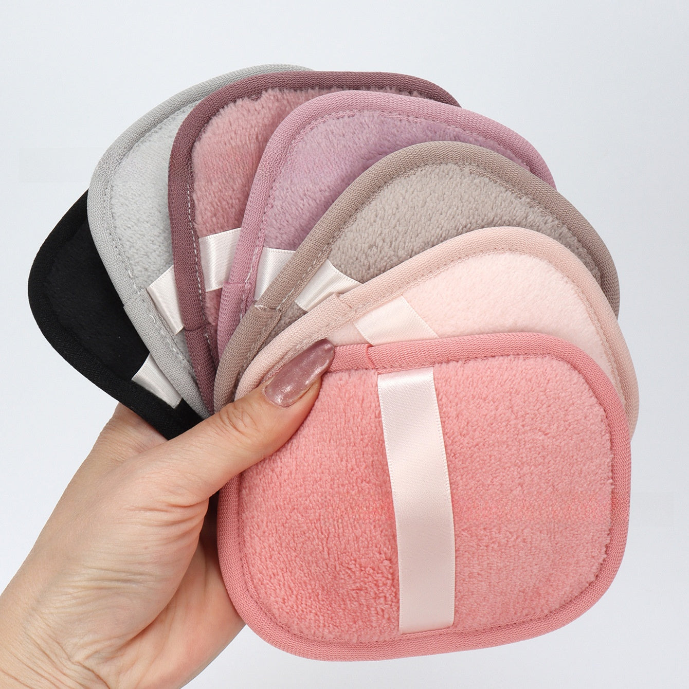 Hand holding a fan of reusable makeup remover pads in pink, gray and mauve shades