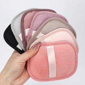 Hand holding a fan of reusable makeup remover pads in pink, gray and mauve shades