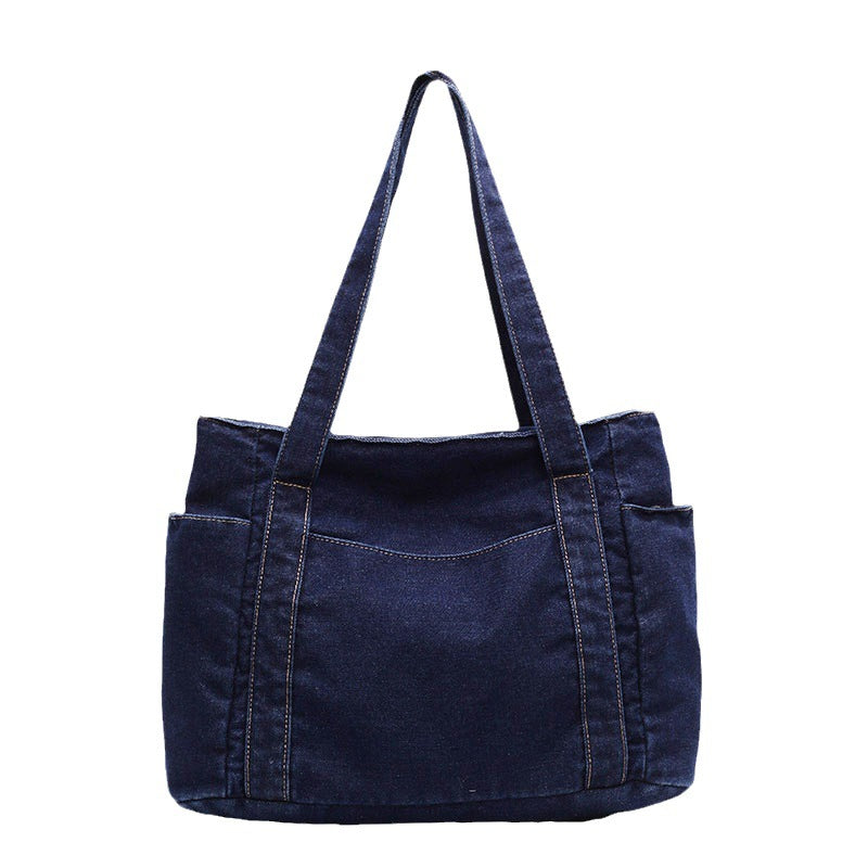 Dark blue denim shoulder tote shown from the back on a white background, twin straps and end patch pockets
