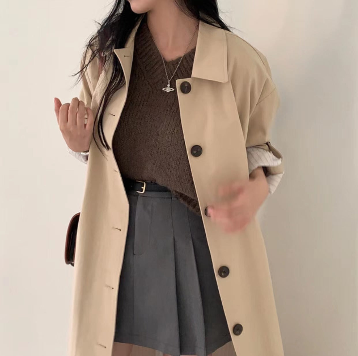 Light khaki long trench coat with lapel collar worn open over a brown knit top