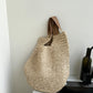 Three quarter view of the woven straw bag hanging near a kitchen counter, rounded body slumped