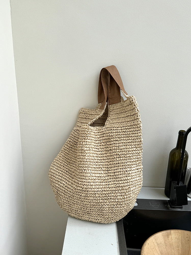 Three quarter view of the woven straw bag hanging near a kitchen counter, rounded body slumped
