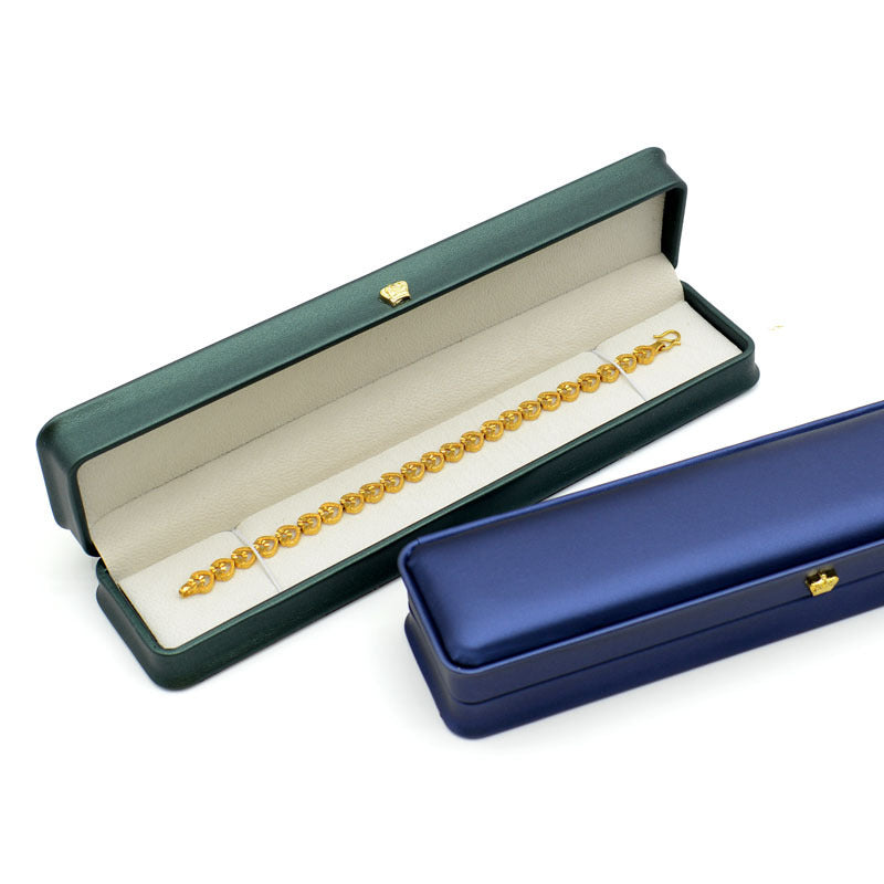 Dark green crown clasp necklace box open with a gold bracelet inside, beside a closed navy box
