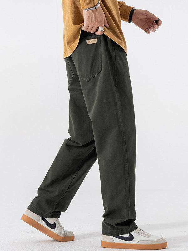 Green straight leg cotton pants seen mid stride with white sneakers and a mustard sweater
