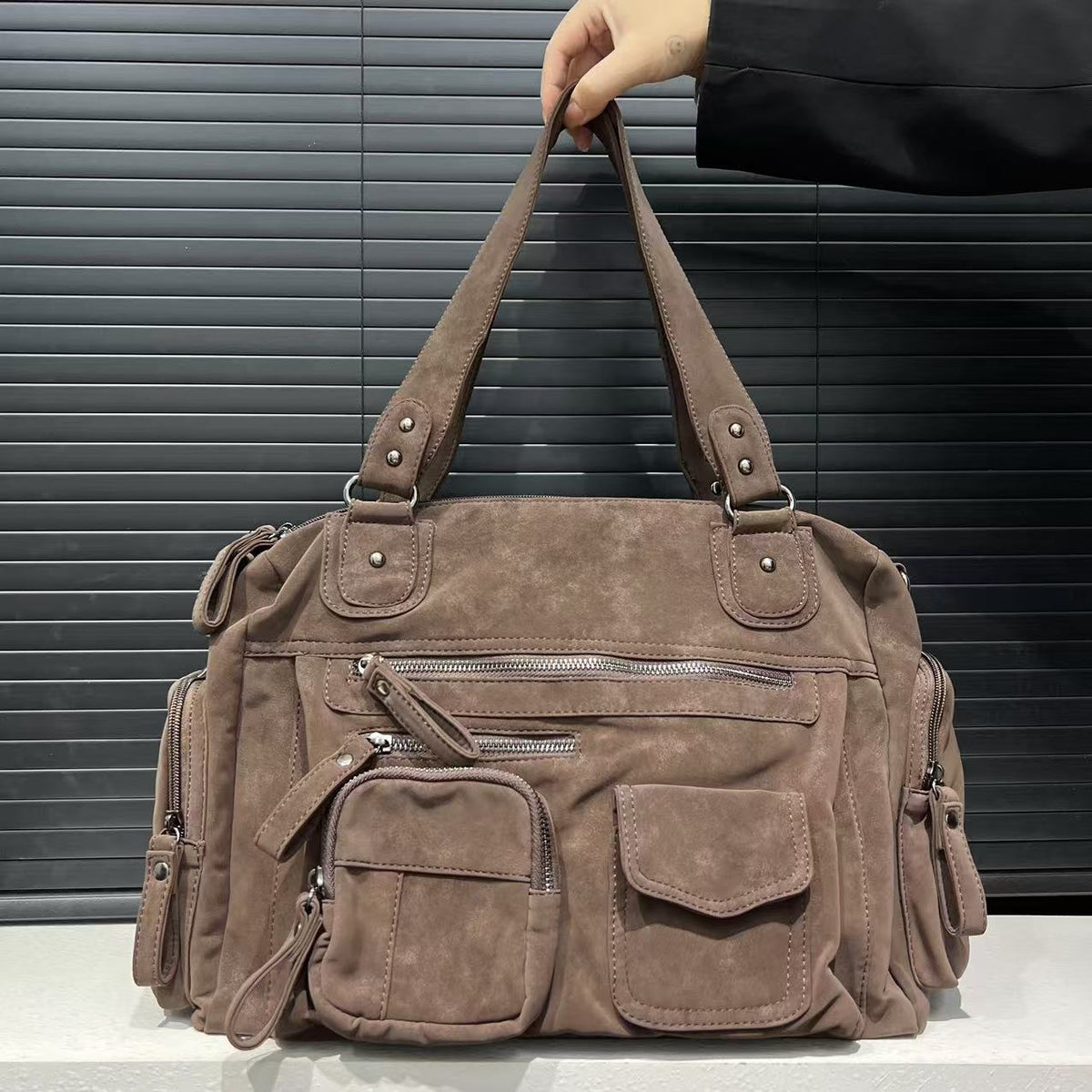 Mocha brown PU shoulder bag held up by its twin handles, front pockets and end zip pockets in view