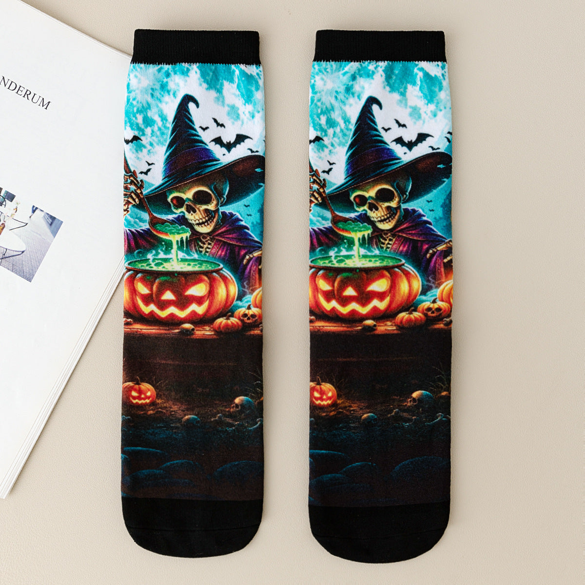 Pair of mid-calf socks printed with a skeleton witch stirring a glowing jack-o-lantern cauldron