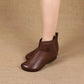 Woman's legs in brown soft leather ankle boots with a side strap and covered button on a woven background