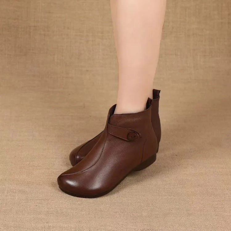 Woman's legs in brown soft leather ankle boots with a side strap and covered button on a woven background