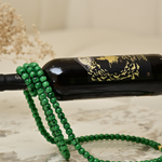 Close view of a green bead strand cradling a wine bottle on a marble surface