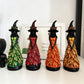 Four witch statues in green, red, orange and yellow leaf gowns lined up on a white shelf