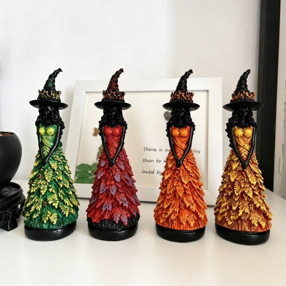Four witch statues in green, red, orange and yellow leaf gowns lined up on a white shelf