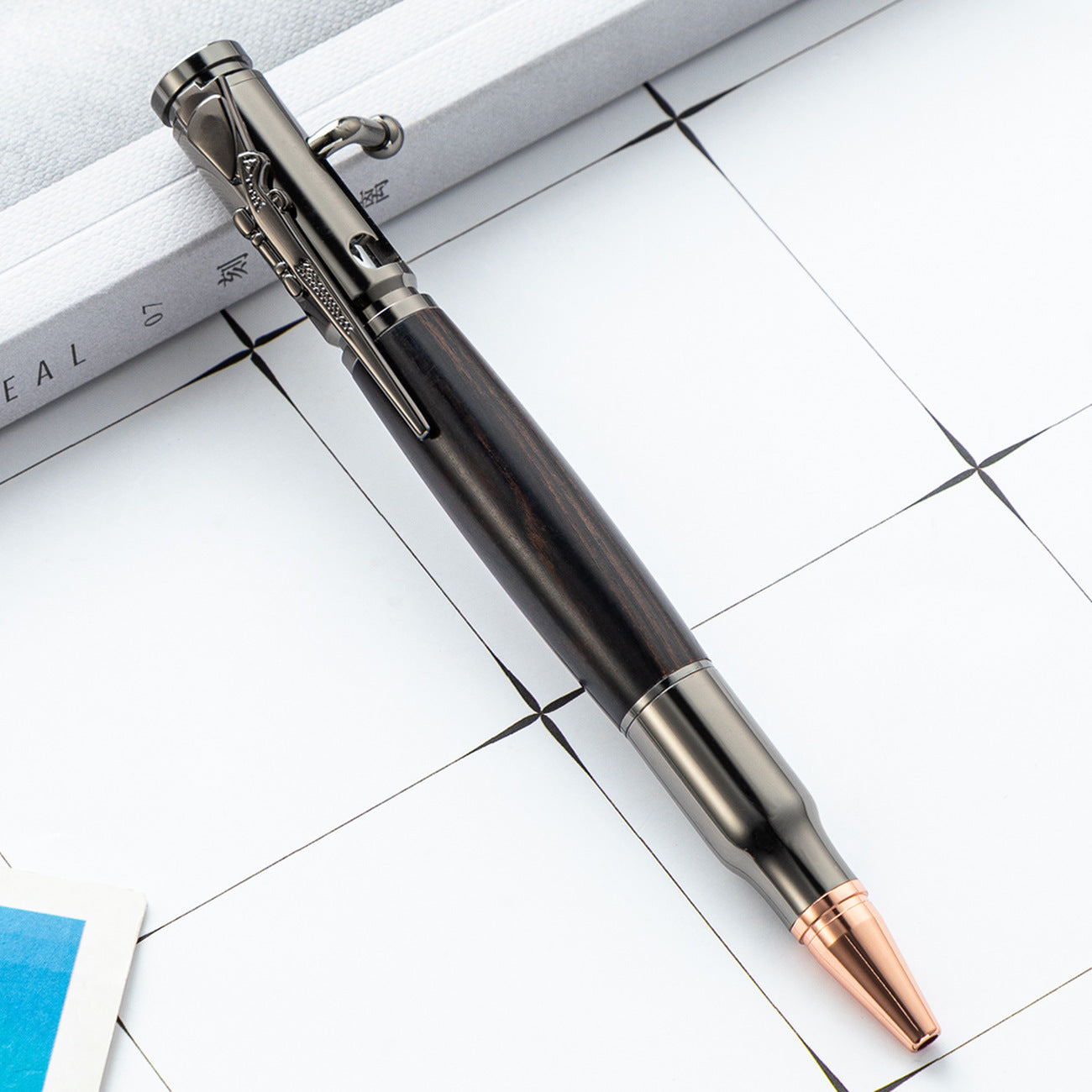 Gunmetal bolt action ballpoint pen with a dark wood barrel and copper toned bullet tip