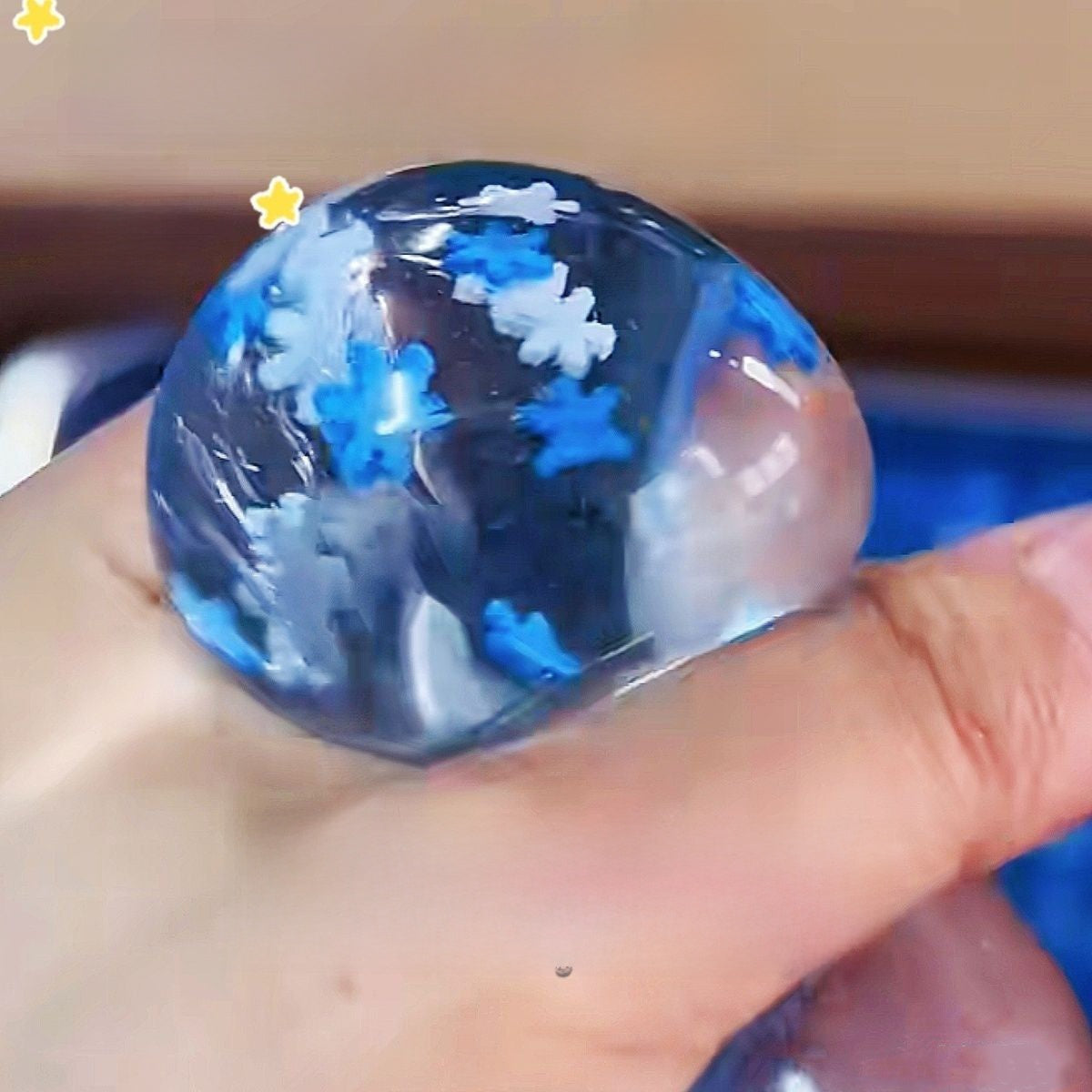 Close view of a clear blue gel cube squishy with white snowflakes suspended in the gel