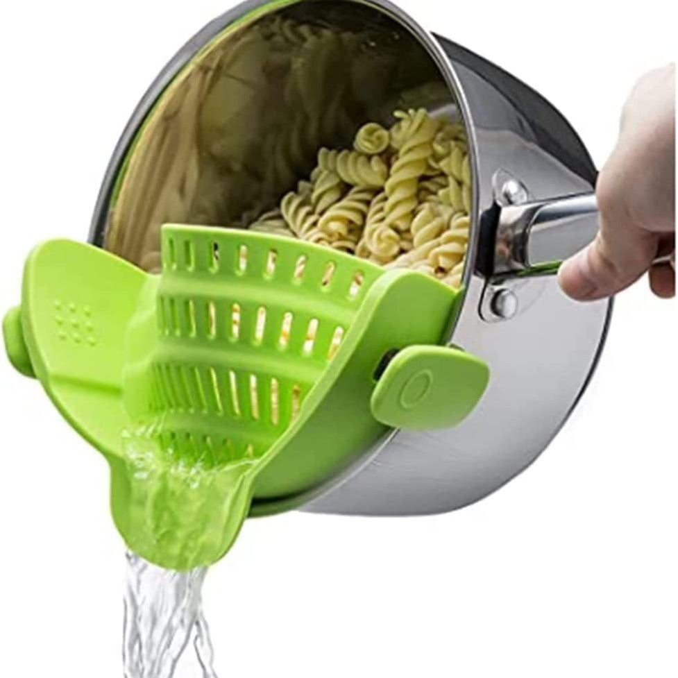 Green silicone clip-on pot strainer on a stainless steel pot draining pasta, water pouring from the spout