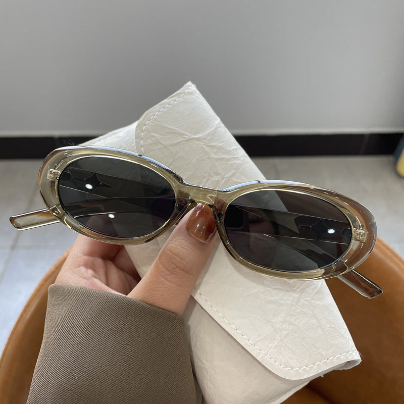 Translucent green oval sunglasses with gray lenses held in a hand beside an off-white case