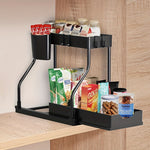 Two tier black under sink pull out storage rack holding jars and packets in a cabinet