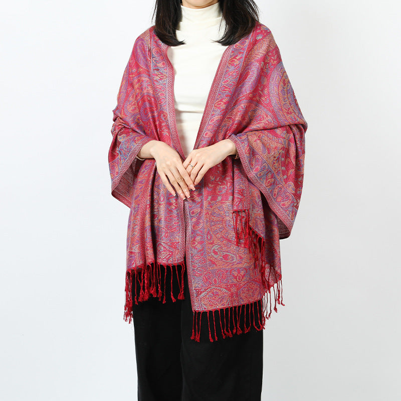 Woman wearing a red paisley shawl with red tassels draped over both shoulders over a white turtleneck