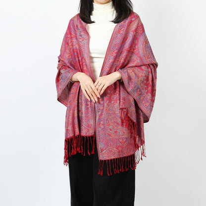 Woman wearing a red paisley shawl with red tassels draped over both shoulders over a white turtleneck