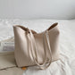 Off-White PU tote bag with two long straps lying on a bed beside a book, Off-White option photo
