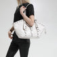 Woman wearing a glossy white hobo shoulder bag on her shoulder, with buckle straps and grommet eyelets