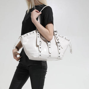 Woman wearing a glossy white hobo shoulder bag on her shoulder, with buckle straps and grommet eyelets