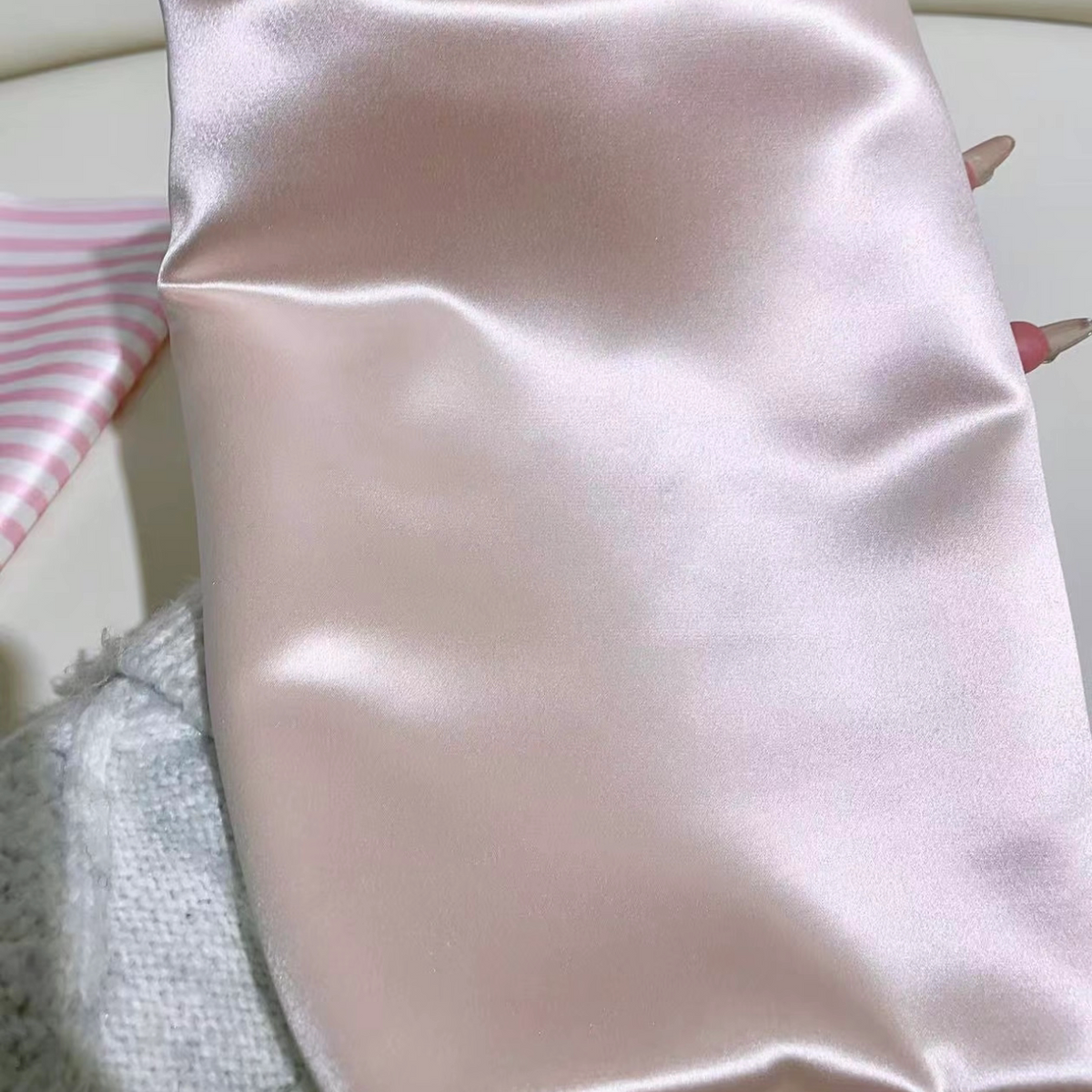 Sakura pink glossy silk pillowcase laid flat beside a pink striped fabric