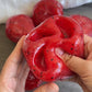 Red fruit gel squishy squeezed by two hands into three deep lobes with a valley between