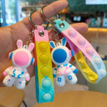 Two soft PVC astronaut rabbit keychains held in a hand with pastel silicone push pop wrist straps