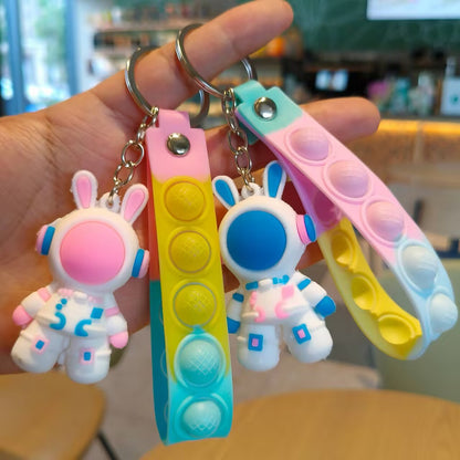 Two soft PVC astronaut rabbit keychains held in a hand with pastel silicone push pop wrist straps