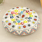 Round cushion with a multicolor flower print on a cream top and a zigzag border, on a beige rug