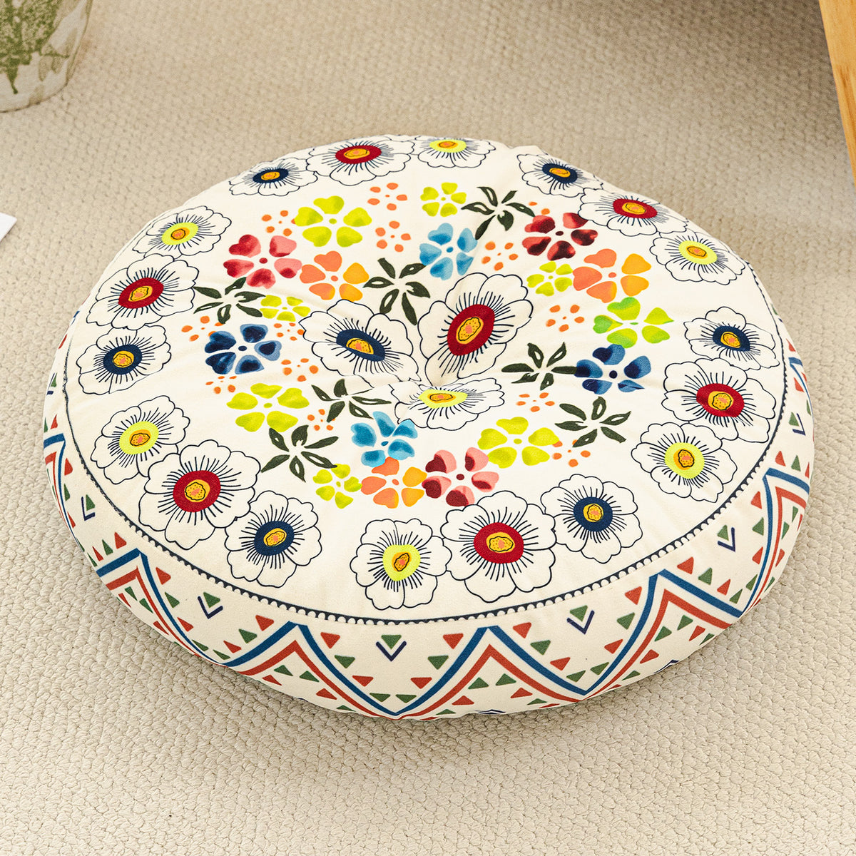 Round cushion with a multicolor flower print on a cream top and a zigzag border, on a beige rug
