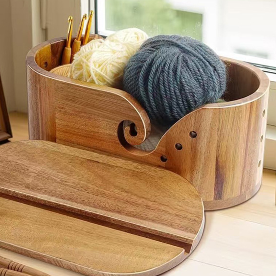 Acacia yarn bowl holding cream and grey yarn balls beside its grooved wooden lid