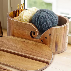 Acacia yarn bowl holding cream and grey yarn balls beside its grooved wooden lid