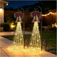 Two Christmas bell yard lights glowing with warm cascading strands beside a garden path at night, solar panels at the base