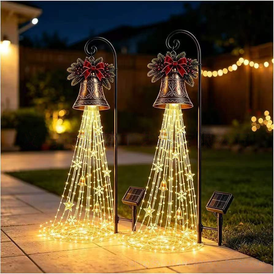 Two Christmas bell yard lights glowing with warm cascading strands beside a garden path at night, solar panels at the base