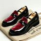 Pair of glossy black loafers with a wine red velvet vamp and a penny strap on a burlap sack