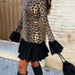 Woman walking in a leopard print mock neck mini dress with black bell cuffs, ruffle hem and tall boots