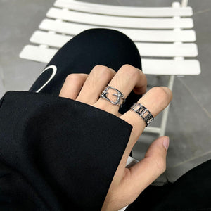 Openwork steel ring on a hand beside a Roman numeral band, styling shot on a white chair