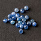 Loose pile of natural blue kyanite round beads on a dark textured background