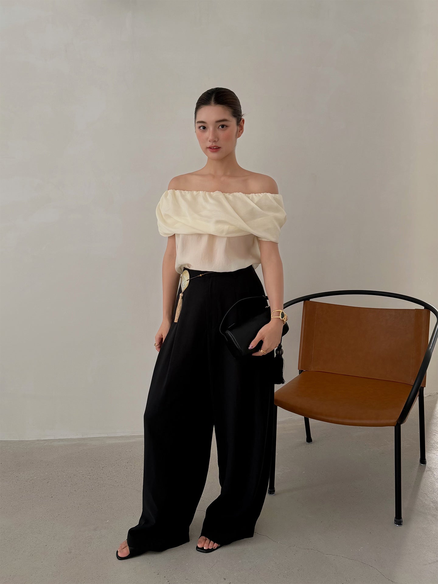 Woman in black high waist wide leg pleated trousers and off shoulder top standing