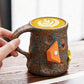 Hand holding a brown and blue speckled ceramic mug of latte with an orange climbing hold decoration on a wooden table