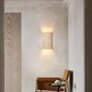 Square travertine stone wall sconce casting up and down light on a pale plaster wall