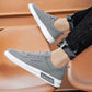 Gray canvas low-top sneaker with white sole worn with ripped black jeans on an orange chair