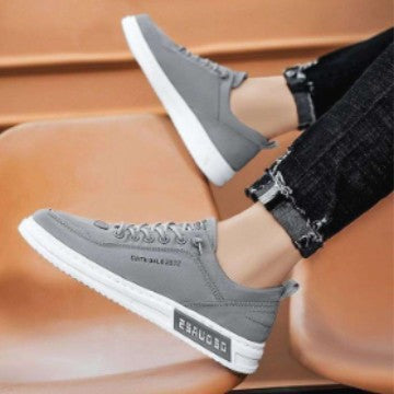 Gray canvas low-top sneaker with white sole worn with ripped black jeans on an orange chair