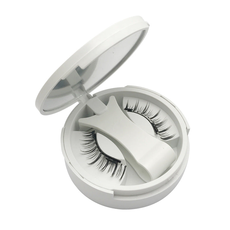 Open white compact holding a pair of magnetic false eyelashes and the clip
